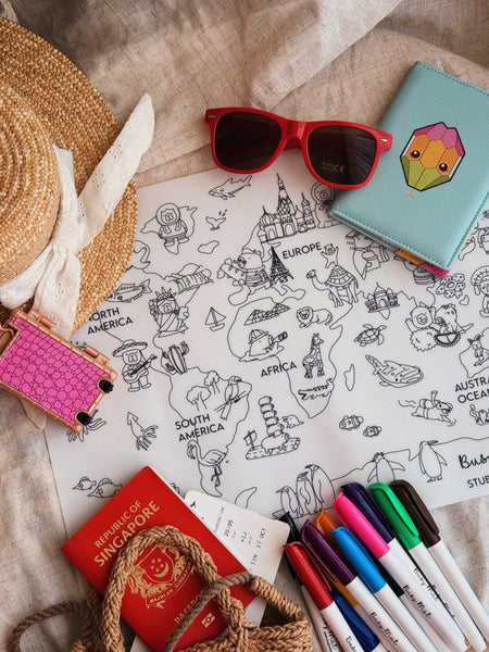 Coloring book with world map, sunglasses, passport, and markers on a textured surface
